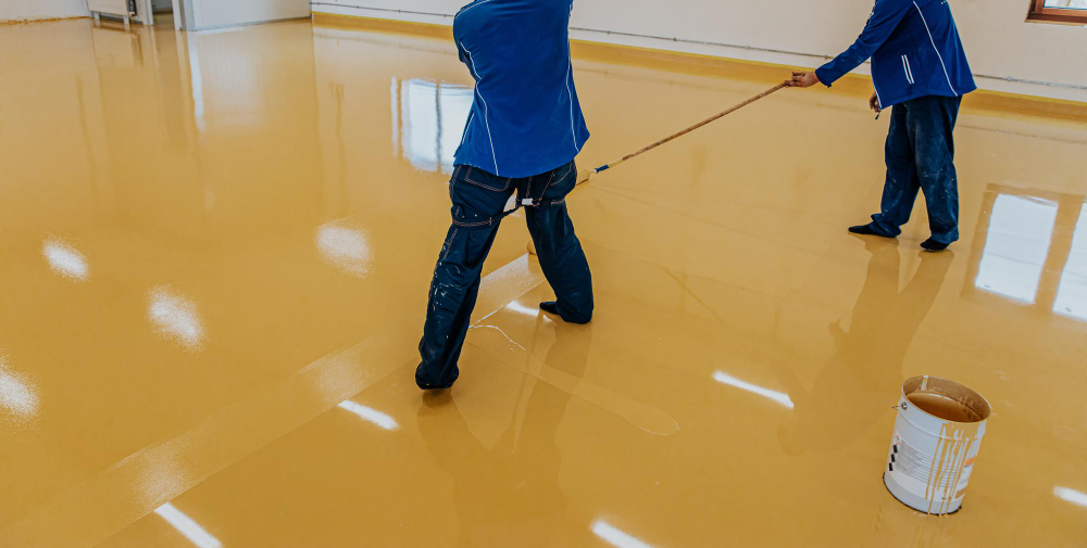 Worker coating floor with selfleveling epoxy resin in industrial workshop