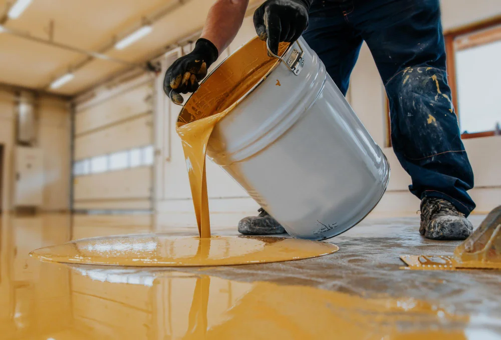 construction worker pouring out epoxy resin from a bucket onto a floor