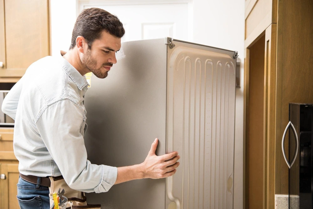 man working as an electrician exposing the back of a fridge to check and repair it