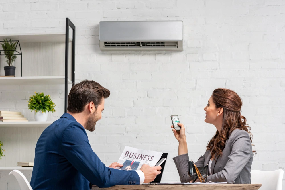 man reading newspaper while sitting at desk near pretty woman holding remote